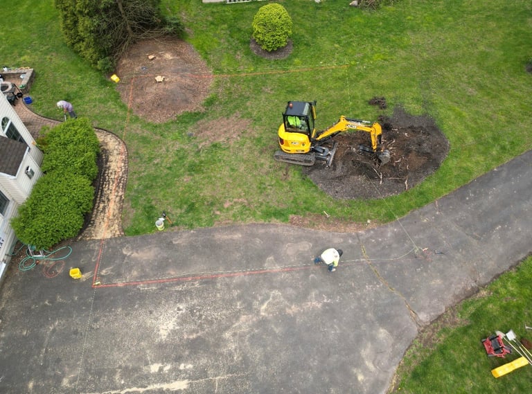 Aerial view of yellow excavator moving soil in residential backyard with driveway and landscaping