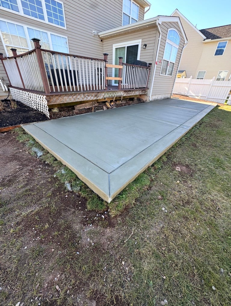 Concrete patio foundation next to residential house with wooden deck and garage door