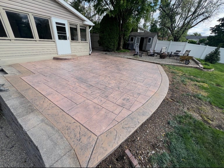 Curved reddish patio attached to white house with lawn and trees in background