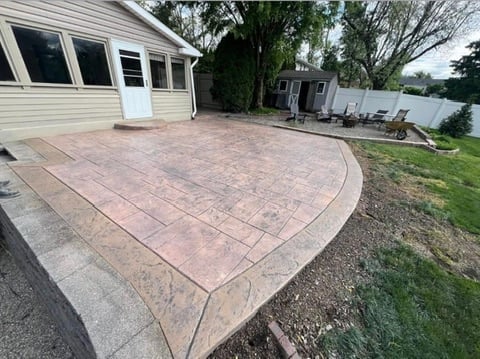 Stamped concrete patio extends from house with landscaping and lawn in background