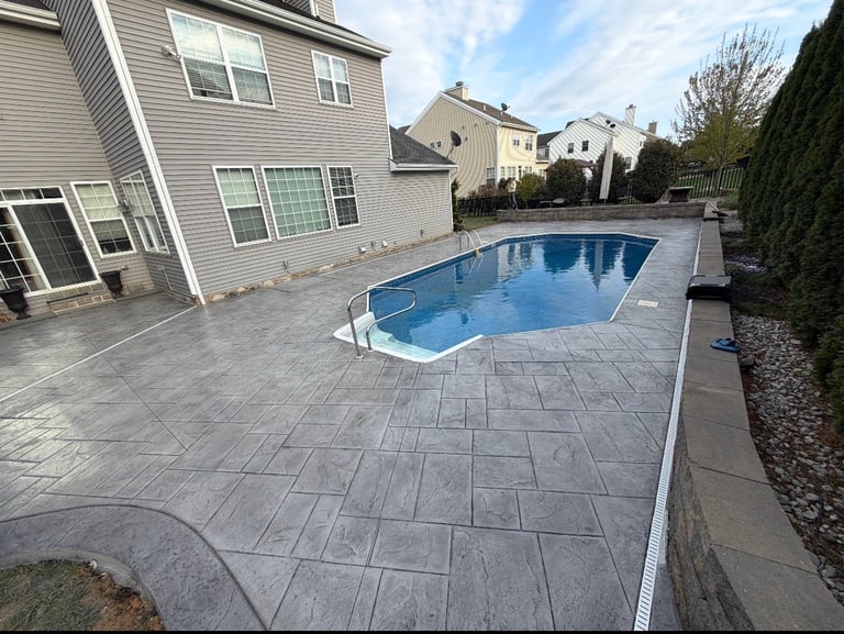 Residential backyard with rectangular swimming pool, paved patio, house, and manicured landscaping