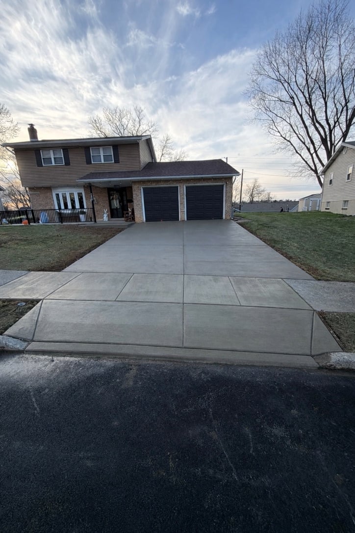 Brown two-story house with two-car garage and concrete driveway on a sunny day with bare trees