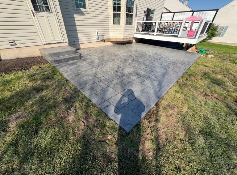 Newly installed gray paver patio in backyard of suburban home with deck and grass surroundings