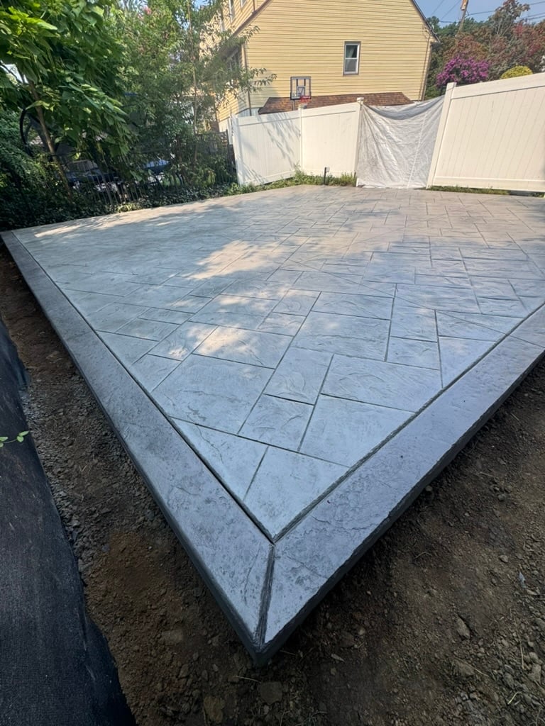 Newly installed blue-gray patio pavers in geometric pattern with white privacy fence and yellow house in background