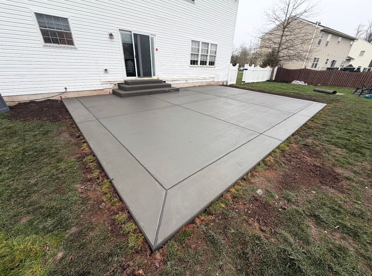 Concrete patio in backyard with white house, glass door, windows, and manicured lawn in background