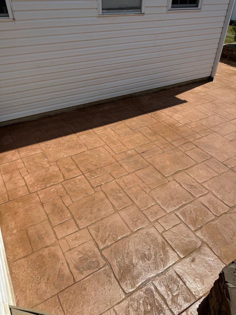 Stamped concrete patio in tan and brown tones adjacent to a light gray house with horizontal siding
