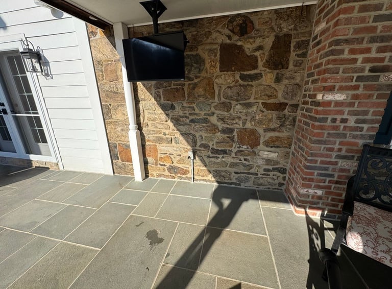 Outdoor patio area with stone and brick walls, flat-screen TV mounted on post, and tiled floor with shadows
