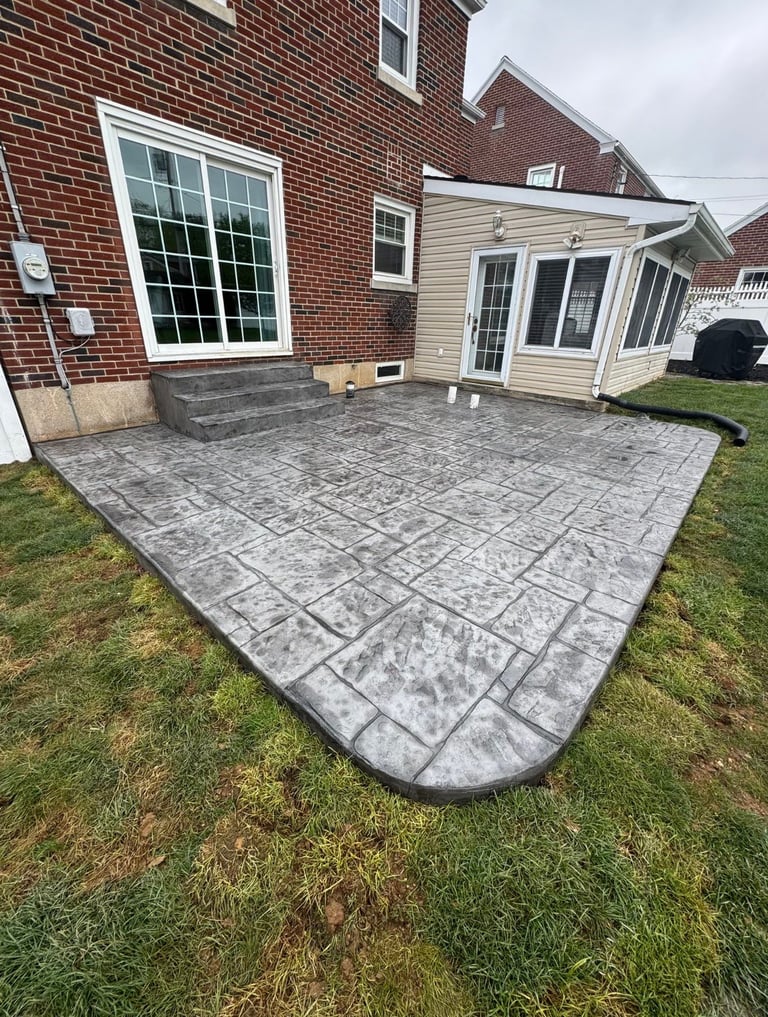 Stamped concrete patio attached to brick home with sunroom and lawn