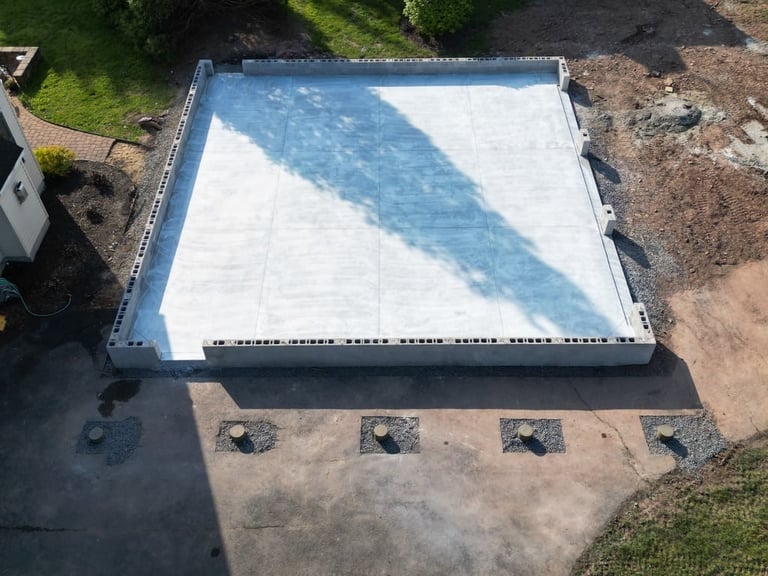 Aerial view of a swimming pool under construction with white surface and blue water feature casting a shadow on the pool deck