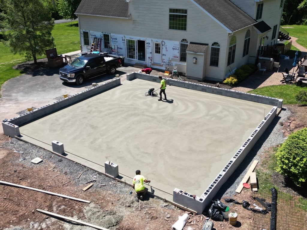 Workers finishing concrete foundation or pad in residential driveway with house and vehicles in background