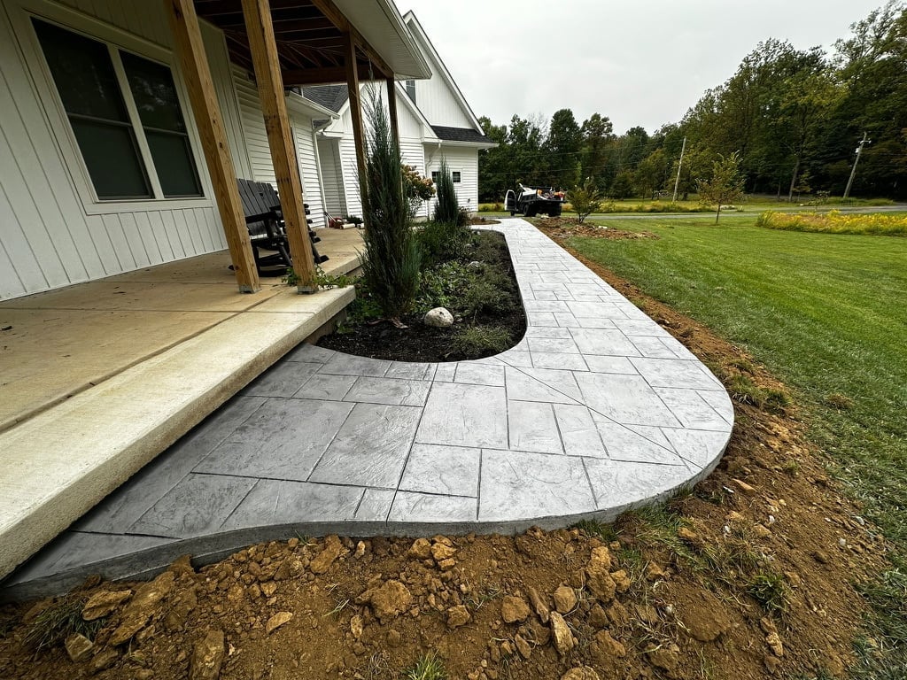 Curved paver patio with topiary shrub extending from a modern farmhouse with white exterior, overlooking open green lawn